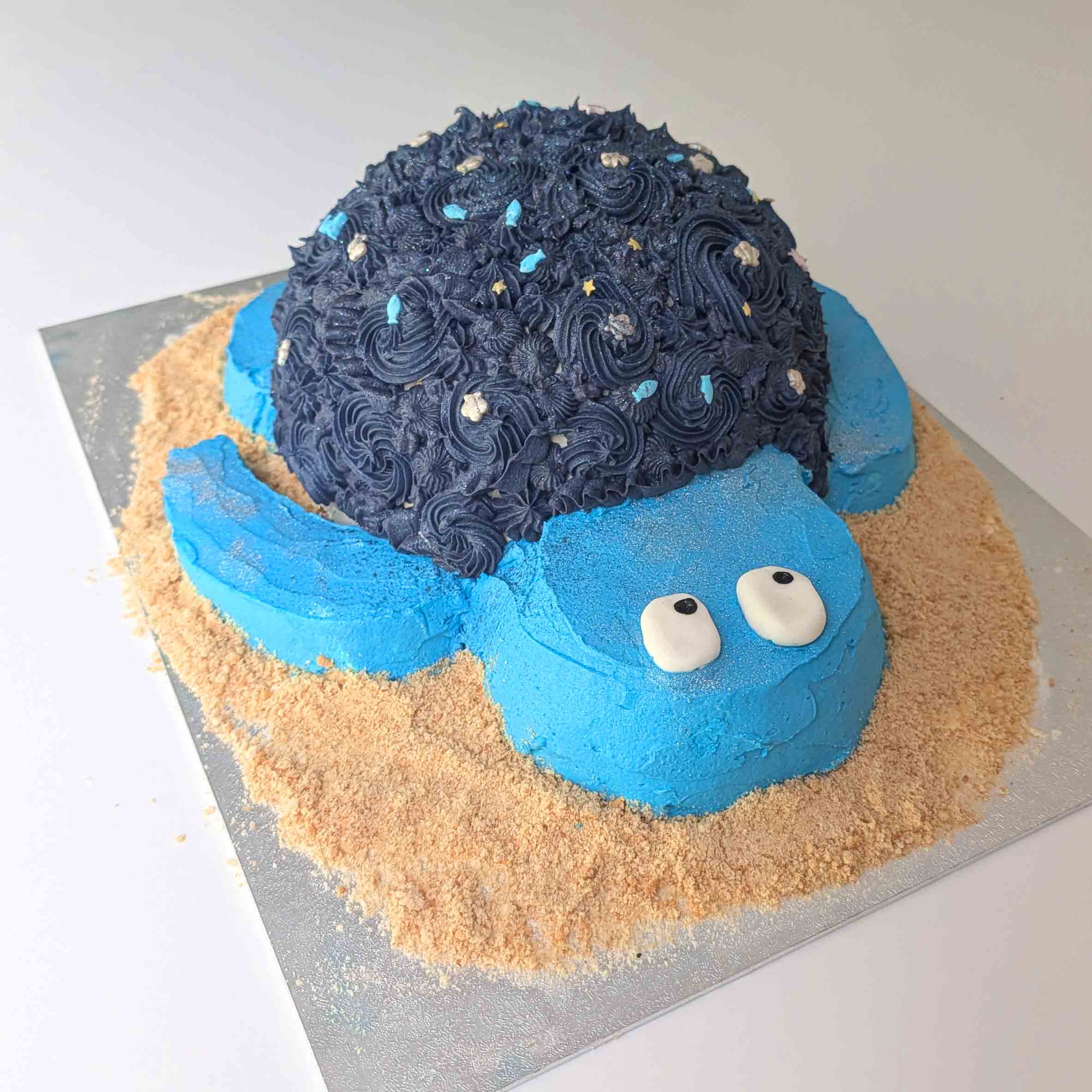 Sea turtle cake with a starry navy shell, set on a biscuit crumb 'sand' base